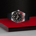 Tudor watch on reflective surface showcases elegant design with black dial and crimson accents.