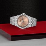 Elegant Tudor watch with rose gold dial and polished stainless steel bracelet on a striking background.
