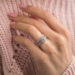 Elegant woman’s hand with sparkling diamond rings on a soft blush background.