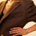 Stylish person in oversized plaid blazer with layered necklaces and elegant bracelets.