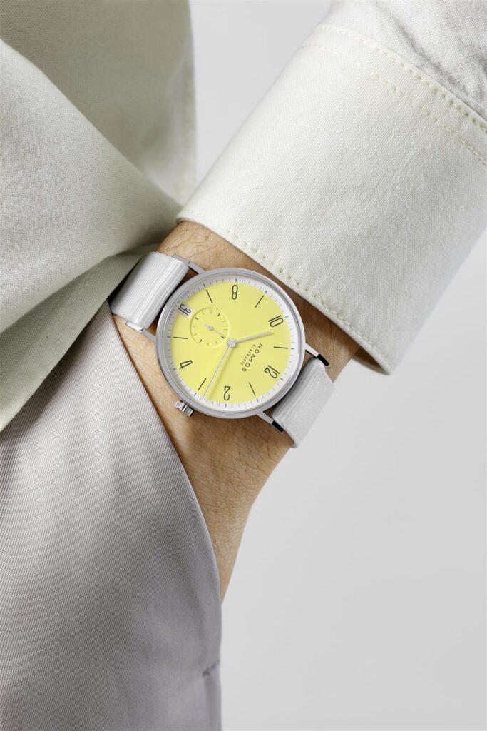 Stylish wrist watch with vibrant yellow dial and gray fabric strap against elegant clothing.