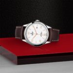 Elegant Tudor watch on a reflective surface, showcasing luxury with a stylish brown leather strap.