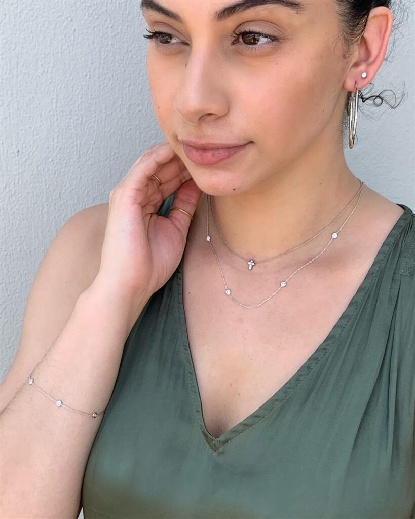 Young woman in olive green top showcasing elegant jewelry against a soft gray background.