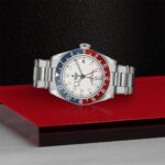 Tudor watch with creamy dial, bidirectional bezel, and stainless steel design resting on glossy surface.