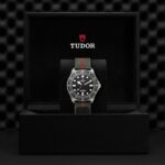 Tudor watch in black box showcases luxury design with sporty green-red strap and luminous dial.