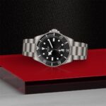 Tudor diving watch with black dial, luminous markers, and unidirectional bezel on textured background.