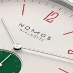 Minimalist NOMOS Glashütte watch with silver dial and bold red hour markers.