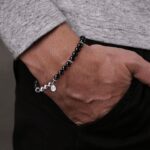 Stylish mens bracelet with black and silver beads on a textured hand against a neutral background.