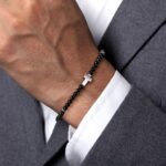 Stylish black bead bracelet with silver cross charm on a well-groomed wrist, fashionable and elegant.