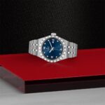 Elegant stainless steel wristwatch with blue dial, bright markers, and luxurious design on a red platform.