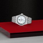 Luxurious stainless steel wristwatch with a mother-of-pearl dial and diamond accents on a vibrant backdrop.