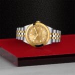Luxurious gold watch with stainless steel bracelet, elegantly displayed on a vibrant red platform.