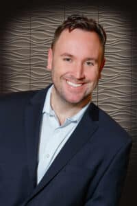 Confident professional man smiling in a smart-casual outfit against a modern textured background.