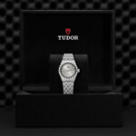 Elegant Tudor watch in luxurious black box, featuring a silver stainless steel band and Roman numerals.