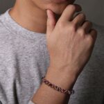 Thoughtful hand gesture under chin, featuring casual attire and stylish bracelet in soft lighting.