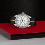 Sleek stainless steel watch with a black leather strap and bold yellow accents on red surface.