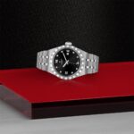 Luxury stainless steel watch on red surface, featuring black dial and diamond indices.