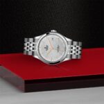 Elegant silver watch with rose gold accents showcased on a striking red and black display.