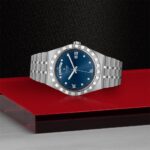 Elegant blue wristwatch with Roman numerals and diamond accents on a stylish textured background.