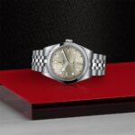 Elegant stainless steel watch displayed on a glossy red platform against a dark background.