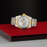 Luxurious Tudor watch with gold accents on a red platform, showcasing elegance and craftsmanship.