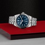 Elegant silver watch with blue dial on textured backdrop, showcasing luxury and style.