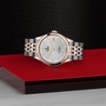 Elegant stainless steel and rose gold luxury watch showcased on a reflective red surface.
