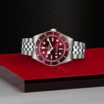 Tudor wristwatch with a striking red dial and stainless steel bracelet on a sleek background.