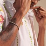 Casual elegance: close-up of tattooed arm adjusting embroidered shirt with stylish silver bracelet.