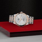 Elegant Tudor watch with stainless steel and rose gold accents on a glossy red surface.