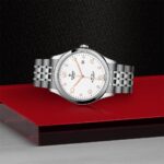 Elegant stainless steel watch on red platform, showcasing luxury and craftsmanship against dark background.