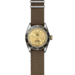 Tudor wristwatch featuring a gold dial, stainless-steel case, and brown textile strap.