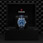 Elegant Tudor watch with blue dial, stainless steel case, and luxurious packaging.