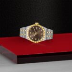 Elegant steel and gold watch with diamond markers on a red and black background.