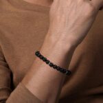 Close-up of a stylish black bead bracelet on a tanned wrist with elegant attire.
