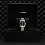 Elegant Tudor watch in luxurious packaging with black dial and gold accents showcased on velvet.