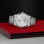 Elegant Tudor watch on a textured black surface, featuring rose gold accents and stainless steel case.