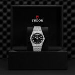 Luxurious Tudor watch in sleek black box, featuring polished silver bracelet and elegant black dial.
