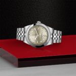 Tudor watch with a gold dial displayed on a vibrant red surface, exuding luxury.
