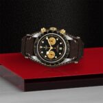 Tudor chronograph watch with black dial, gold accents, and leather strap on modern display.