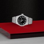 Elegant stainless steel watch with black dial on a vibrant red background.