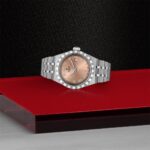 Elegant stainless steel watch with rose gold dial on a vibrant red background.