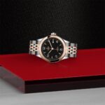 Elegant Tudor watch with black dial and rose gold accents on a striking red backdrop.