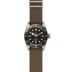 Tudor luxury watch featuring a black dial, gold accents, unidirectional bezel, and brown textile strap.