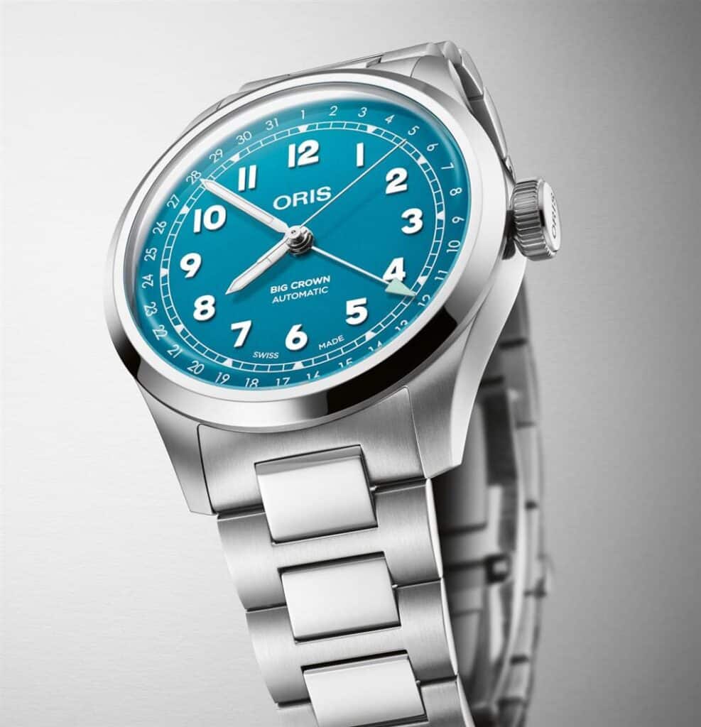 ORIS watch with turquoise dial, oversized crown, and stainless steel bracelet for stylish functionality.