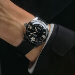 Sleek divers watch on a wrist, featuring a black dial, luminescent markers, and rubber strap.
