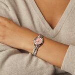 Elegant silver watch with pink dial on a well-groomed wrist against soft gray fabric.
