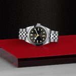 Elegant stainless steel watch with black dial and golden accents on a glossy red platform.