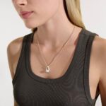 Young woman in dark gray top showcases elegant pearl necklace with silver chain.