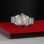 Elegant stainless-steel watch on a vibrant red surface, showcasing timeless design and luxury craftsmanship.